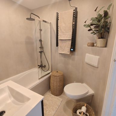 Moderne badkamer met douche, bad, toilet en planten in een lichte, neutrale stijl.